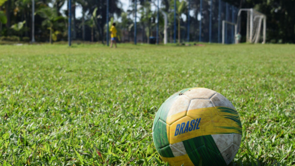 Bola de futebol branca, verde e amarela com a escrita “Brasil”, em um campo de futebol